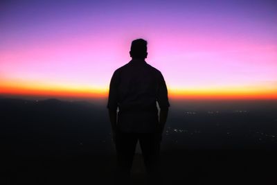 Silhouette man standing on landscape against sunset sky