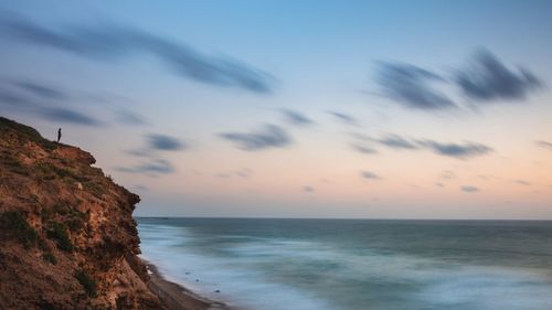 Cliff by sea against sky during sunset