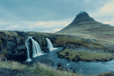 Scenic view of waterfall against cloudy sky