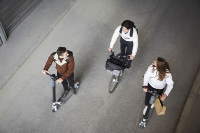 High angle view of male and female friends riding electric push scooters and bicycle on road in city