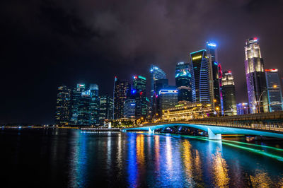 Illuminated buildings by river against sky at night