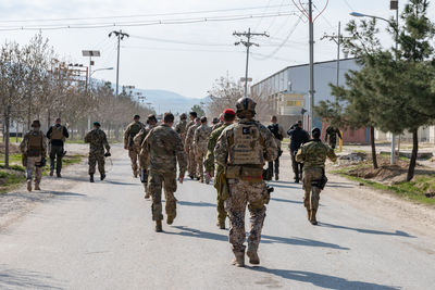 Rear view of army soldiers walking on road in city