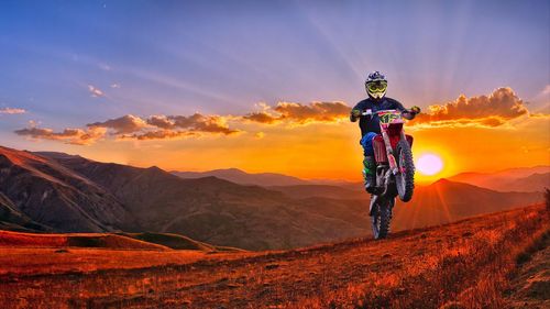 Man riding bicycle on mountain against sky during sunset