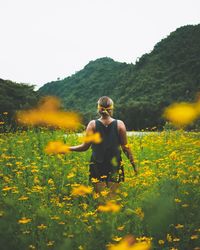 Rear view of shirtless young woman with yellow flowers in field