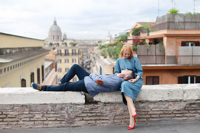 Couple sitting on wall against city