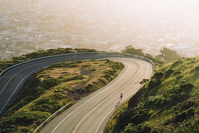 Aerial view of winding road on mountain against cityscape during sunset