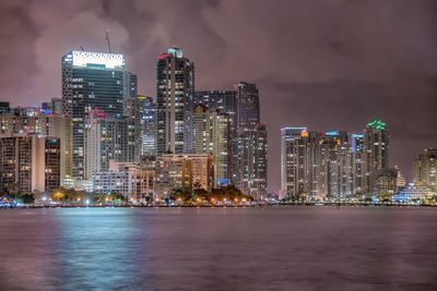 Sea and illuminated buildings against cloudy sky