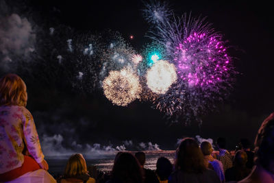 People looking at firework display during night