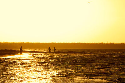 Silhouette people on sea against clear sky during sunset