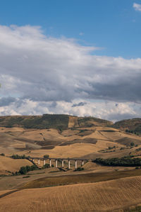 Distant image of bridge over agricultural landscape against cloudy sky