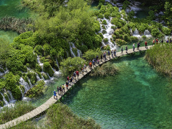 People crossing walkway above waterfall lakes