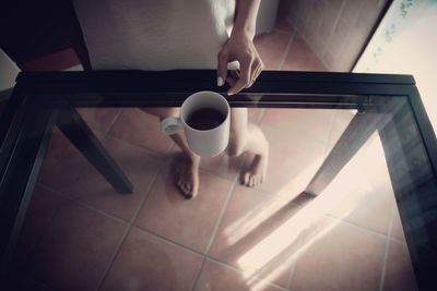 Low section of woman standing by coffee on glass table at home