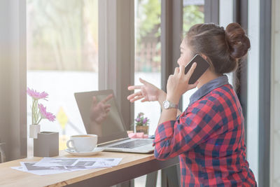 Rear view of woman using mobile phone while sitting on table at home