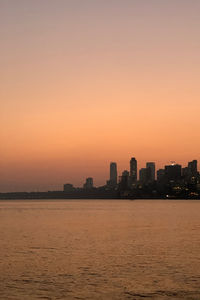 Silhouette buildings by sea against sky during sunset in mumbai, india.