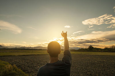 Rear view of man standing on field against sky during sunset