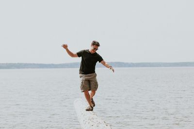 Man walking on fallen tree over sea against sky