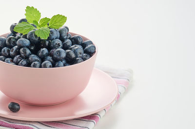 Ripe blueberry in a pink ceramic plate on a white table, tasty and useful berry, copy space