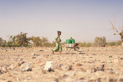 Full length of girl pushing wheelbarrow on land