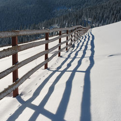 Shadow of railing on snow covered field