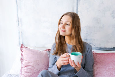 Attractive brunette woman is sitting on bed in her pajamas drinking hot tea or