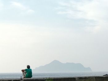 Rear view of man looking at sea against sky