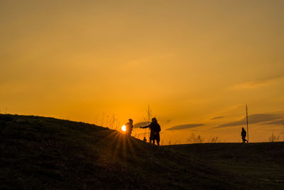 Silhouette people on field against sky during sunset