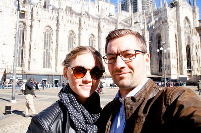 Portrait of couple standing against milan cathedral on sunny day