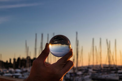 Close-up of hand holding crystal ball against sky during sunset