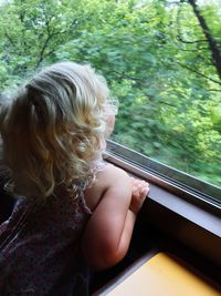 Rear view of girl looking through window of train