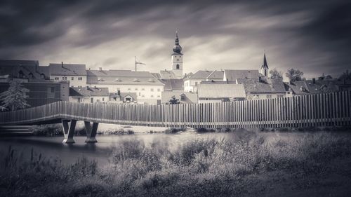 Buildings by river against cloudy sky