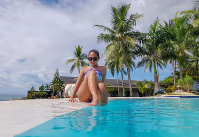 Young woman in bikini at swimming pool against sky