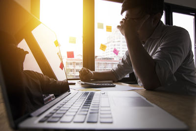Close-up of laptop on desk against stressed businessman at office during sunset