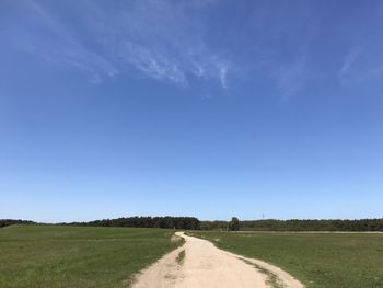 Dirt road amidst field against blue sky