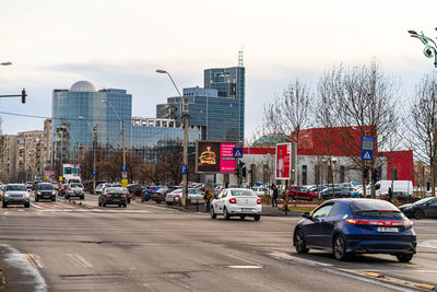 Cars on city street by buildings against sky