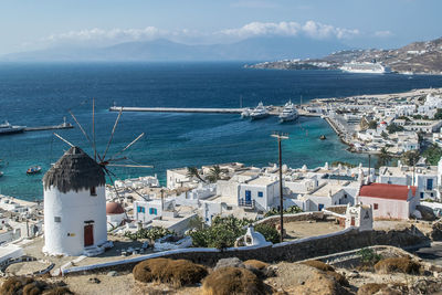 High angle view of windmill and cityscape of mykonos, greece. mediterranean sea w buildings on coast