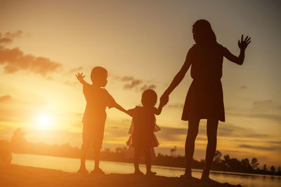 Silhouette of mother and daughter on beach against sky during sunset