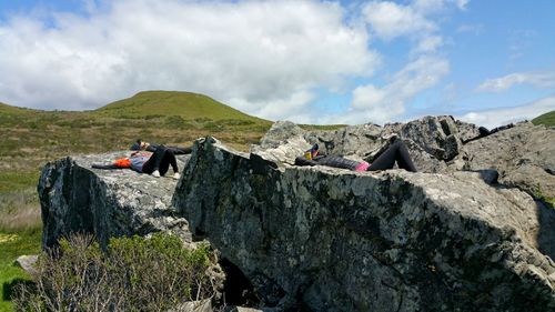 People on relaxing rock against sky