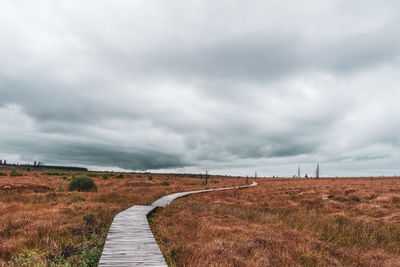 Empty footpath amidst field against sky