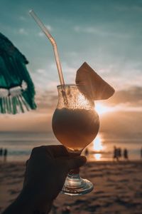 Close-up of hand holding drink against sky at sunset