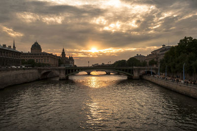 Bridge over river against buildings in city at sunset