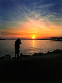 Silhouette man photographing sea against sunset sky