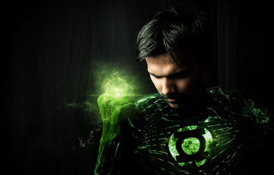 Man in superhero costume with green light against black background