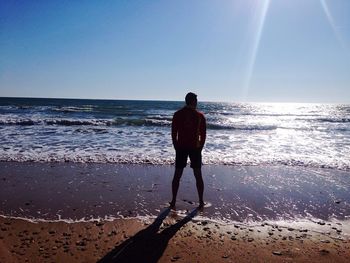 Rear view full length of man standing at beach against sky on sunny day