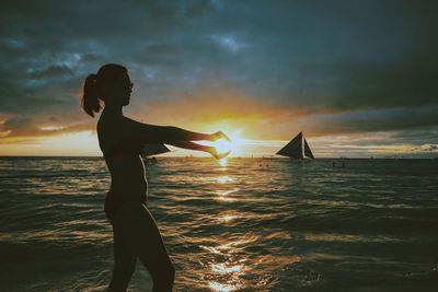 Silhouette of woman standing on beach during sunset