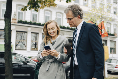 Smiling businesswoman showing smart phone to male coworker in city