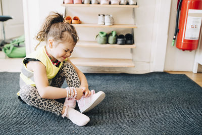 Full length of girl making face while sitting on carpet wearing shoes in cloakroom at child care