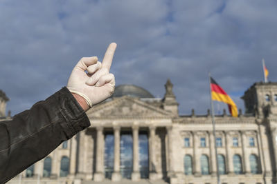 Hand holding flag on city against cloudy sky