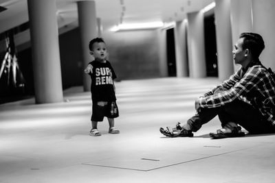 Full length of young man sitting by son on floor