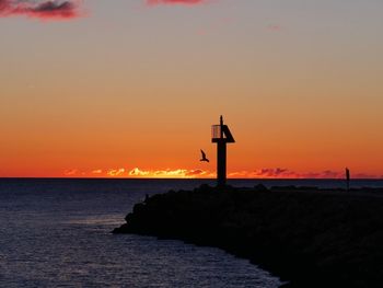 Silhouette lighthouse by sea against sky during sunset