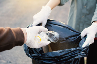 Cropped hand wearing protective glove while putting plastic bottle in bag